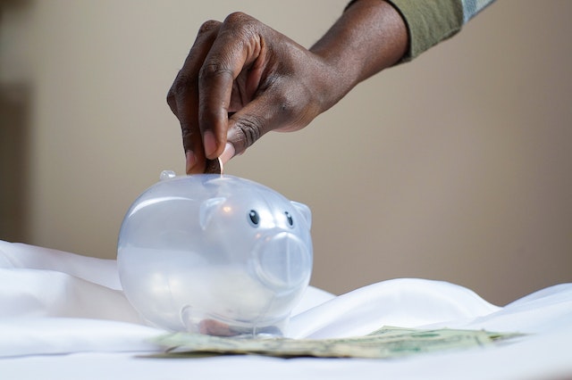 person putting money in clear piggy bank